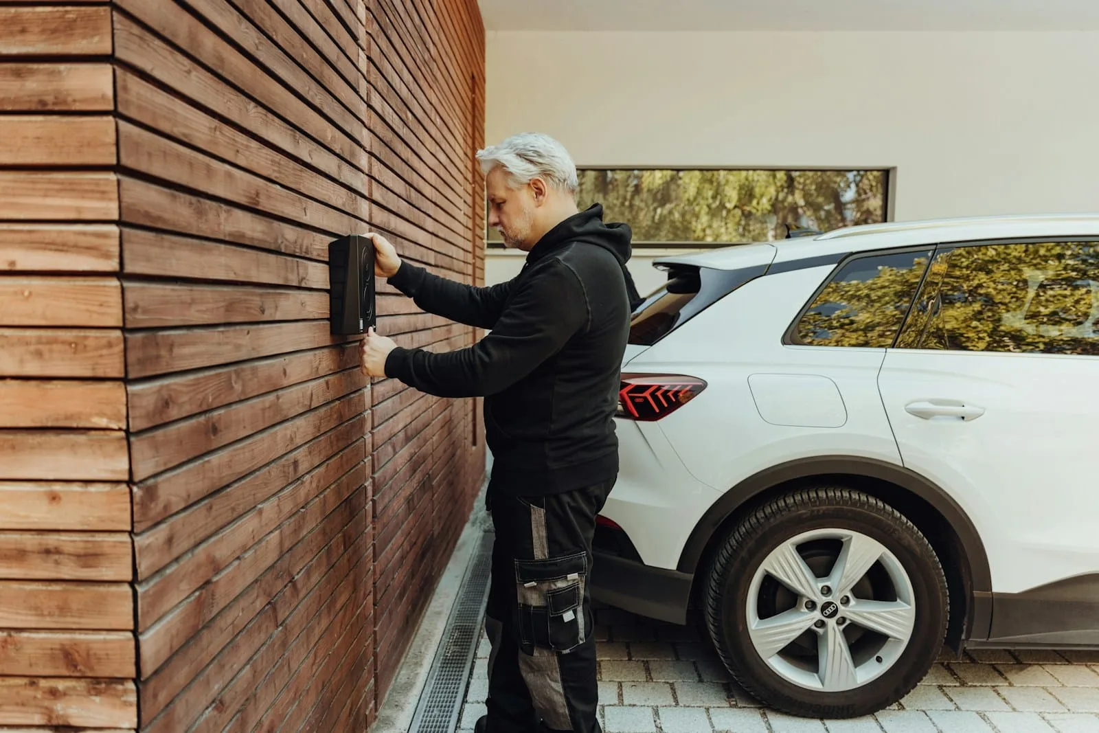 Mann nimmt eine Wandladestation neben einem Elektroauto in Betrieb